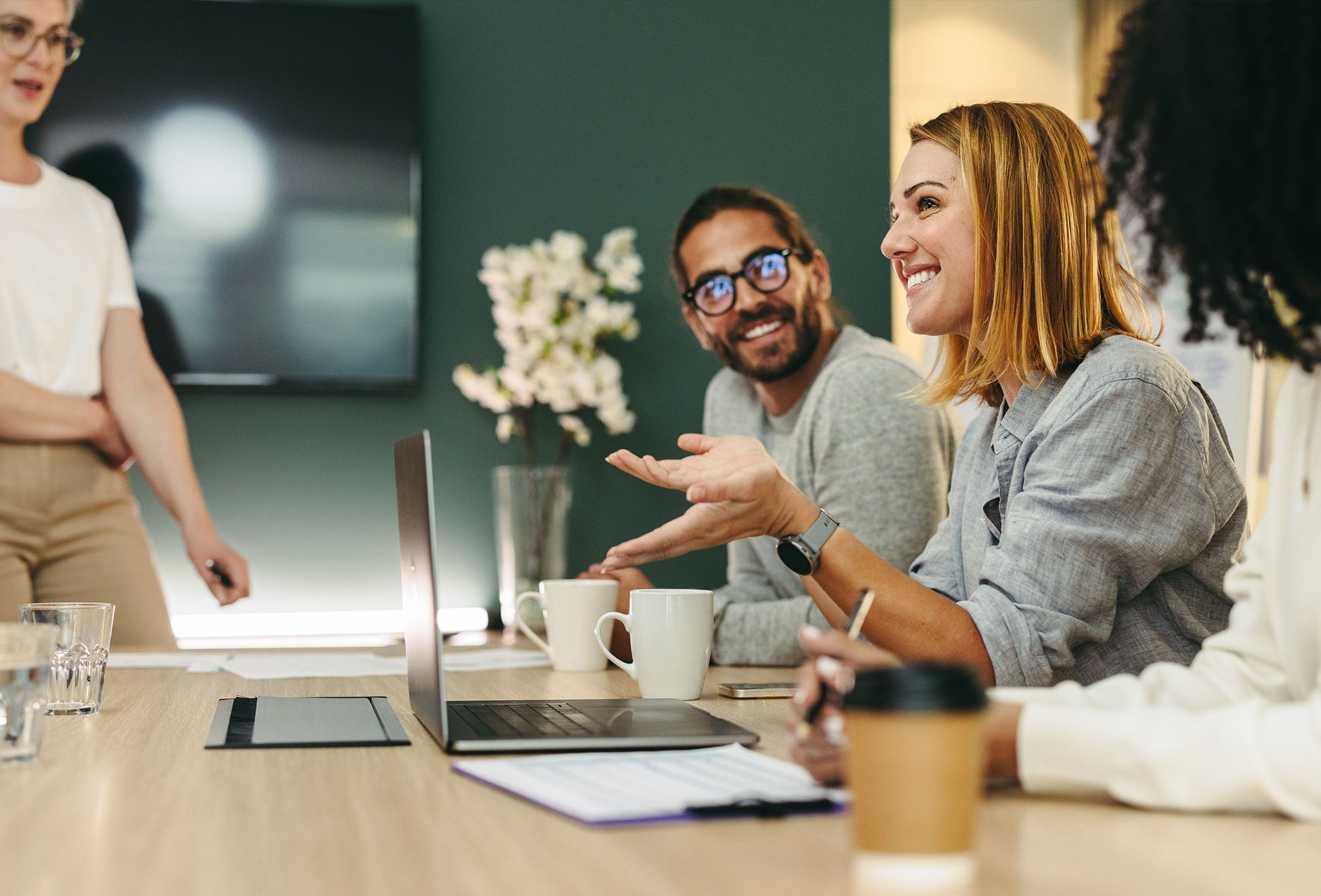 Coworkers in a meeting, smiling and engaged as one woman speaks, creating a collaborative and positive workplace atmosphere.