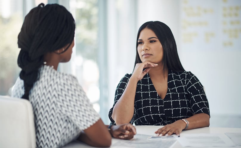 Two women having a focused conversation in a bright office setting, with one actively listening and thoughtfully engaging.