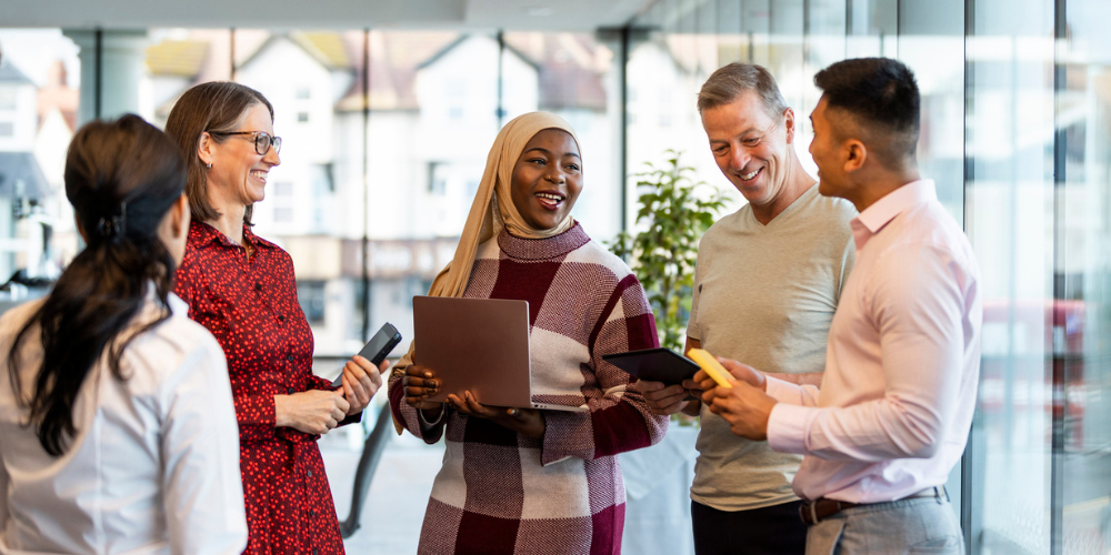 Diverse group of colleagues smiling and talking together in a bright, modern office setting.