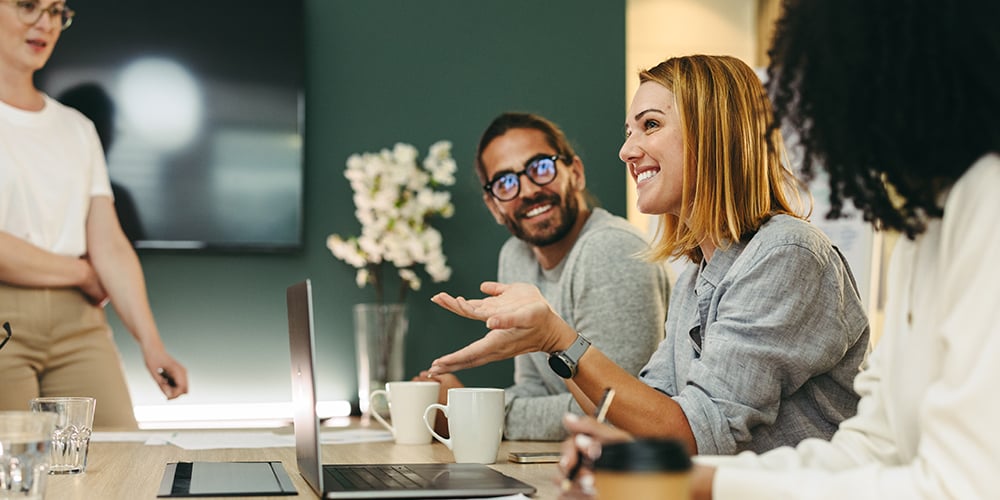Coworkers in a meeting, smiling and engaged as one woman speaks, creating a collaborative and positive workplace atmosphere.