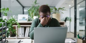 Stressed employee at a cluttered desk, head in hands, suggesting overwhelm and exhaustion, highlighting signs of workplace burnout.