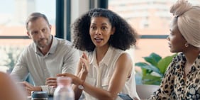 Woman speaking confidently while colleagues listen attentively in a modern meeting room.