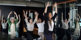 Group of employees of varying ages engaged in a stretching activity with arms raised.