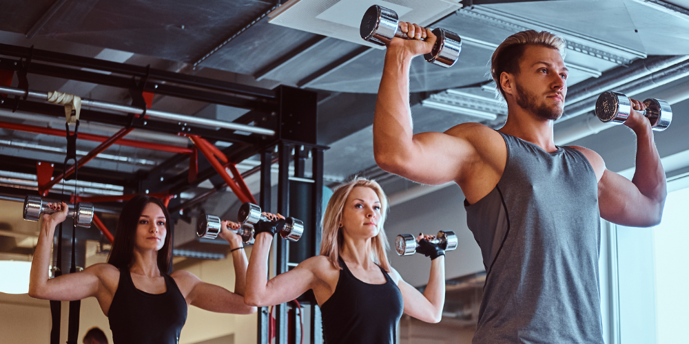 Group fitness class lifting dumbbells overhead in a modern gym during strength training