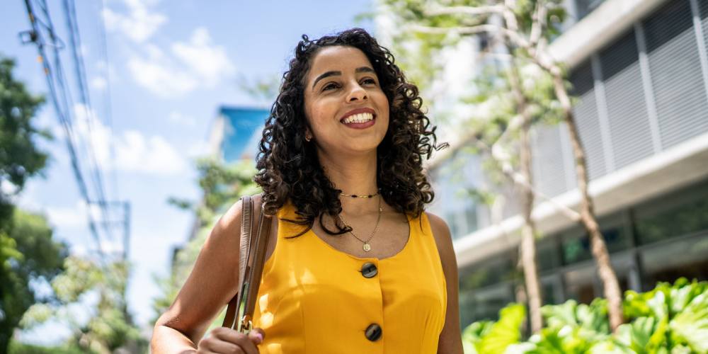 Professional woman smiling outdoors in sunlight, symbolizing the benefits of unplugging from work and recharging outside the office.