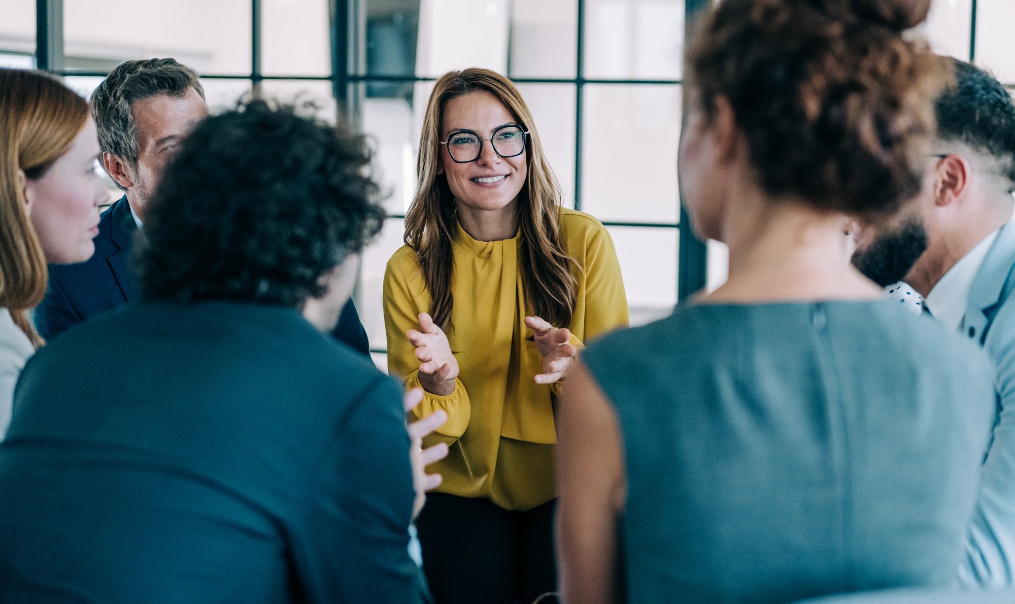 Leader facilitating an engaged team discussion in a modern office, with colleagues listening and contributing in a collaborative setting.
