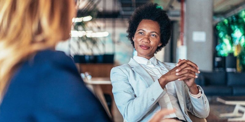 Confident woman in a light blazer seated in a relaxed conversation, conveying professionalism and thoughtful engagement.