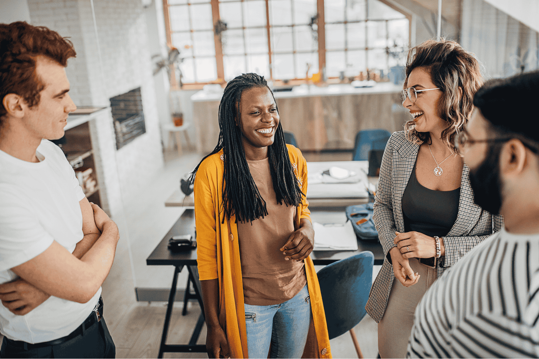 Group of colleagues standing together in a relaxed office setting, laughing and enjoying a light-hearted conversation.